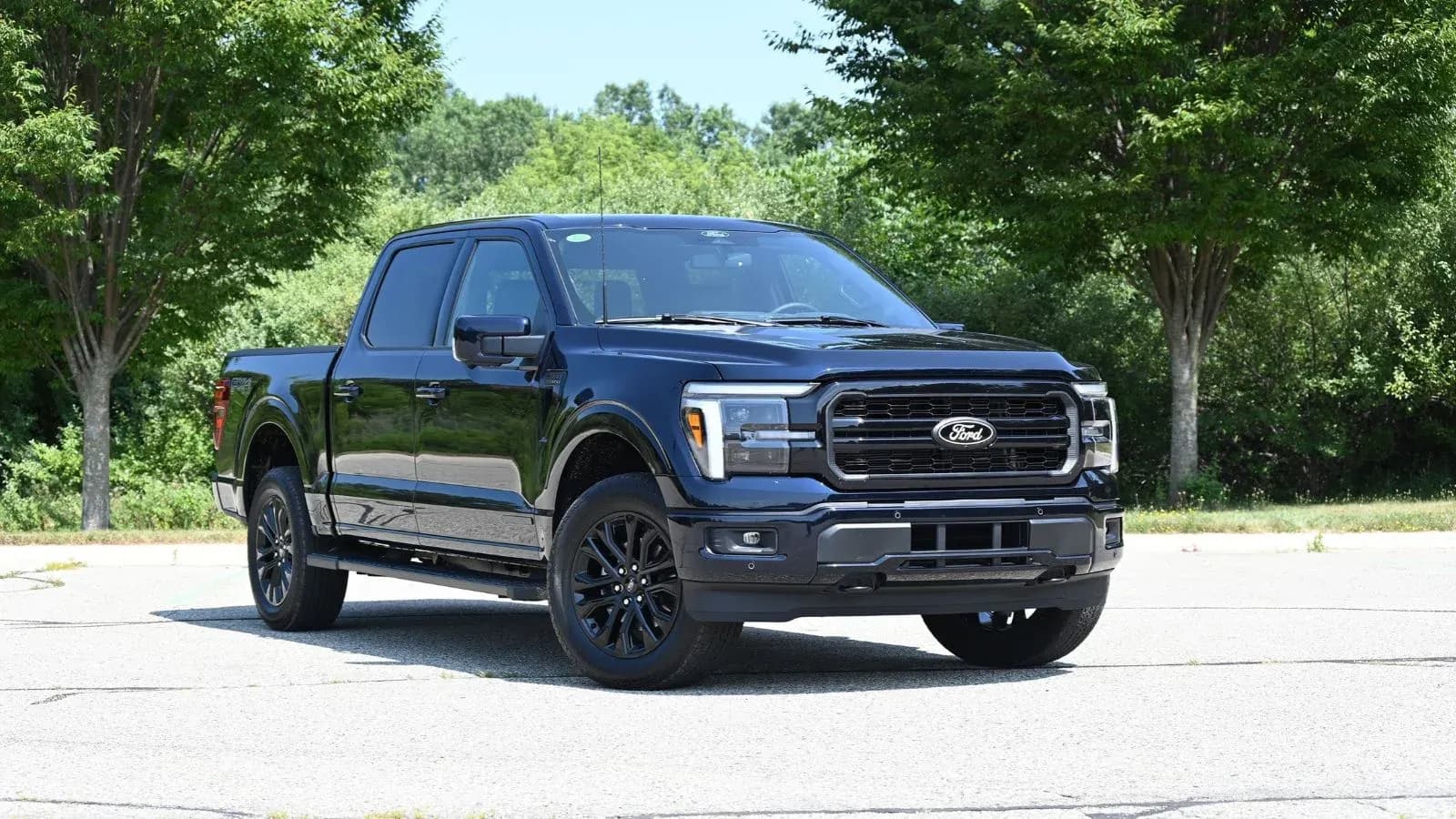 A 2026 Ford F-150 Powerboost Hybrid is parked at an angle in a parking lot against a landscaped background