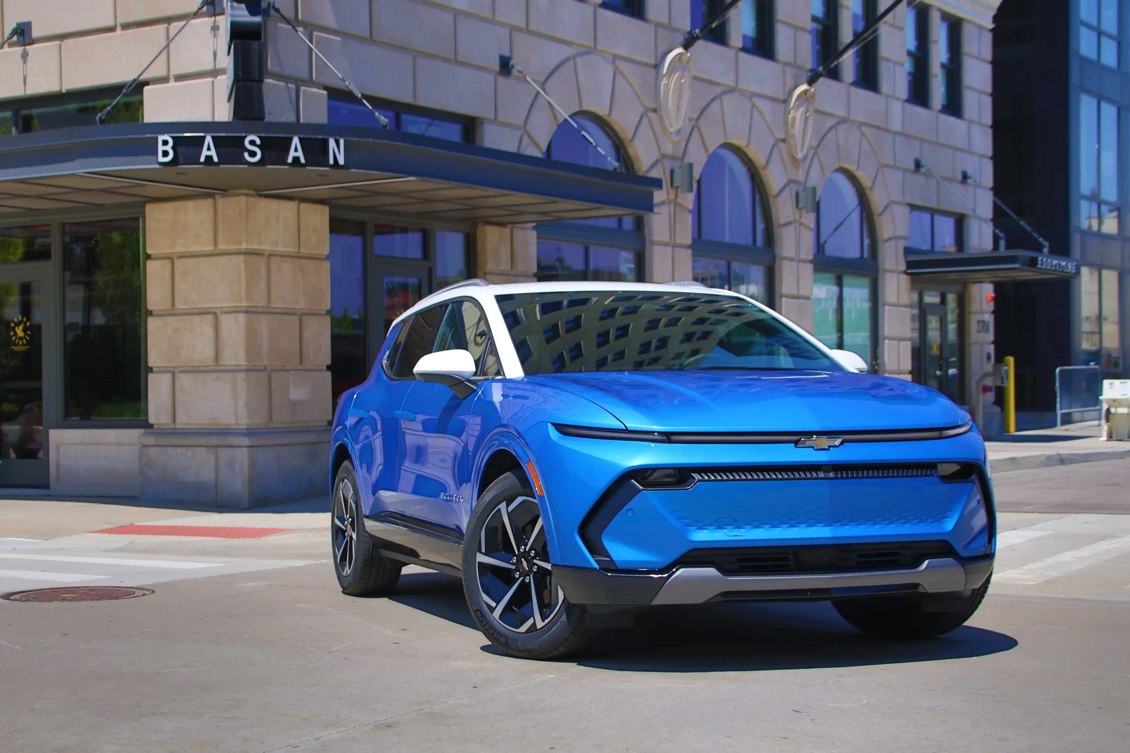Blue 2027 Chevrolet Equinox EV front angle with large multicolored compass in the background