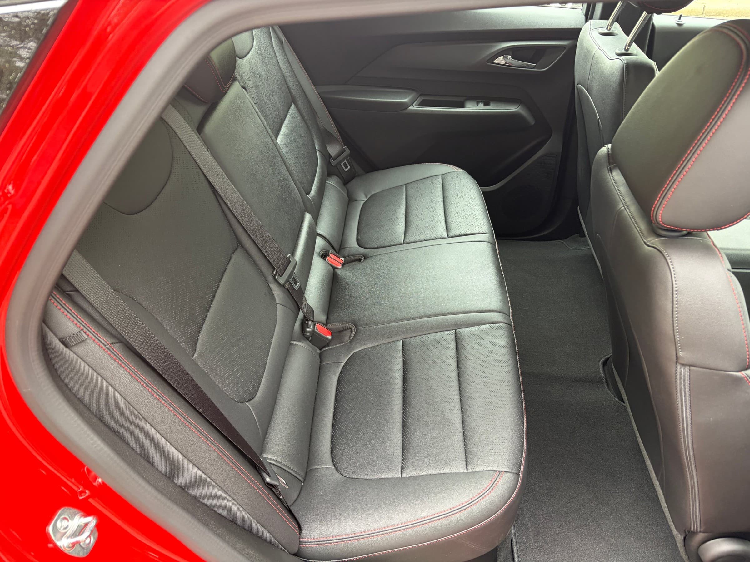 Rear seat of a Chevrolet Bolt seen through the open back door, with black perforated upholstery and red contrast stitching.