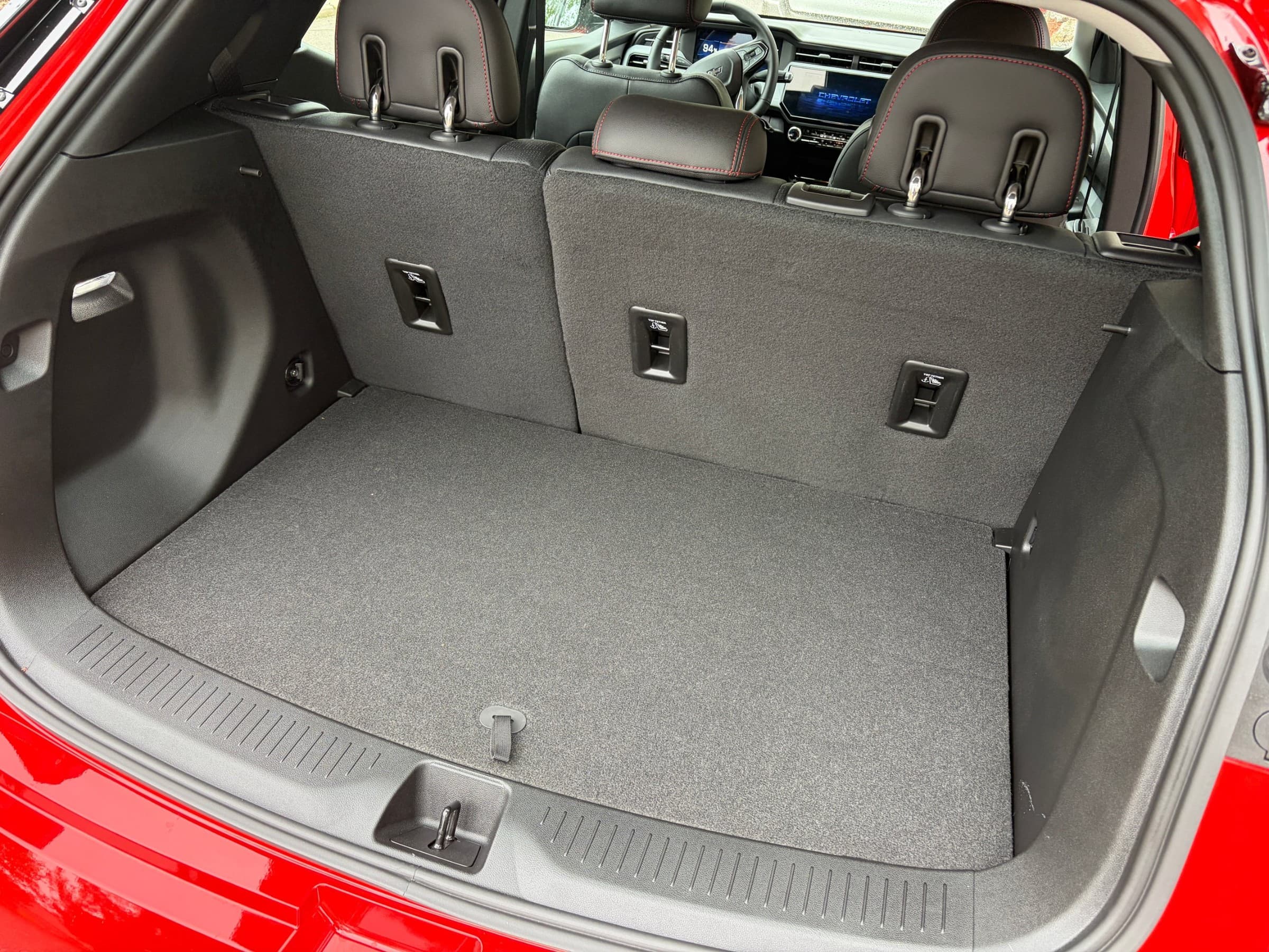  Cargo area of a Chevrolet Bolt with the hatch open, showing a flat gray carpeted floor and upright rear seatbacks.