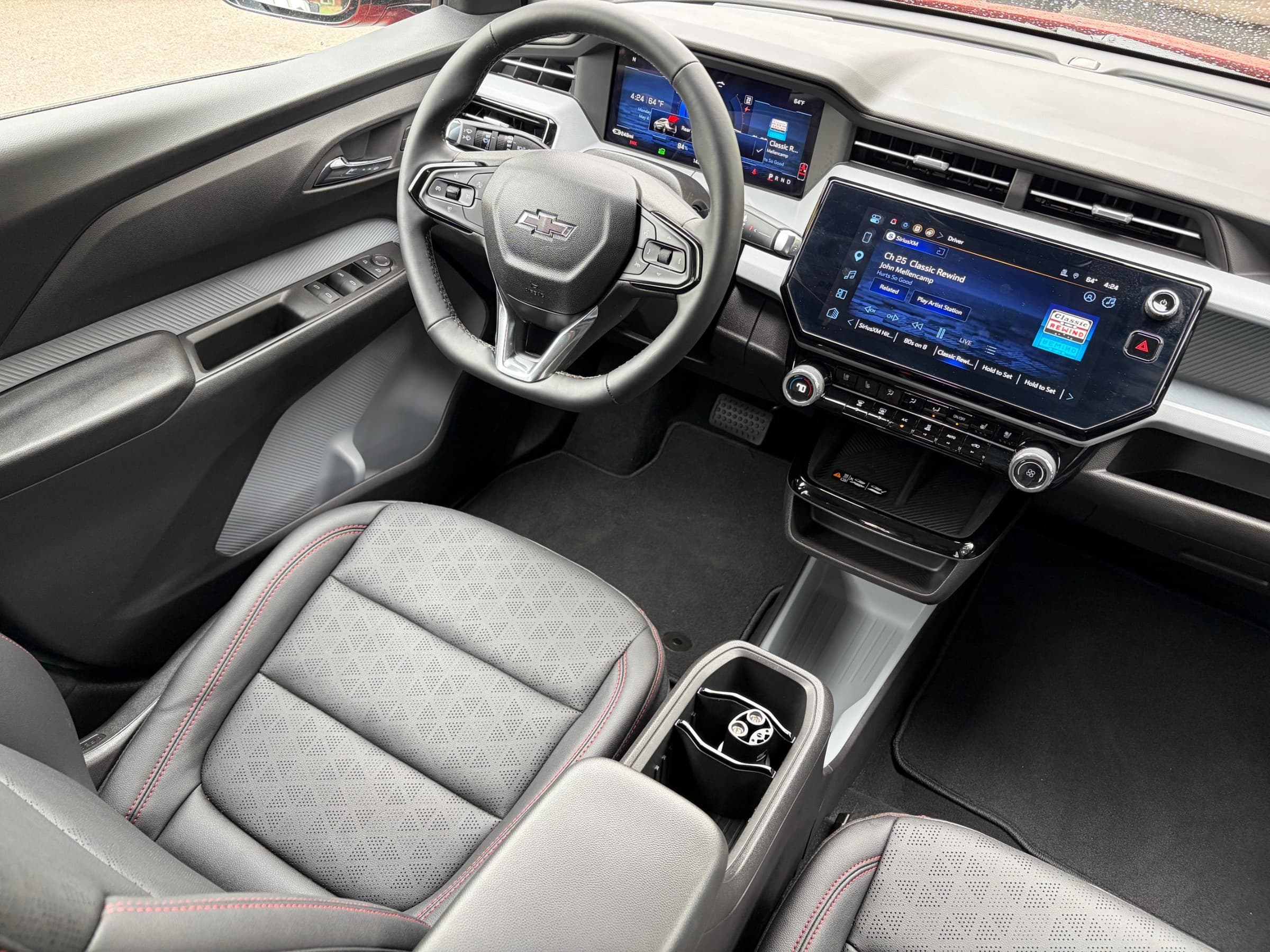 Overhead view of the Chevrolet Bolt cabin showing the steering wheel, digital gauge cluster, large center touchscreen and black seats with red stitching.
