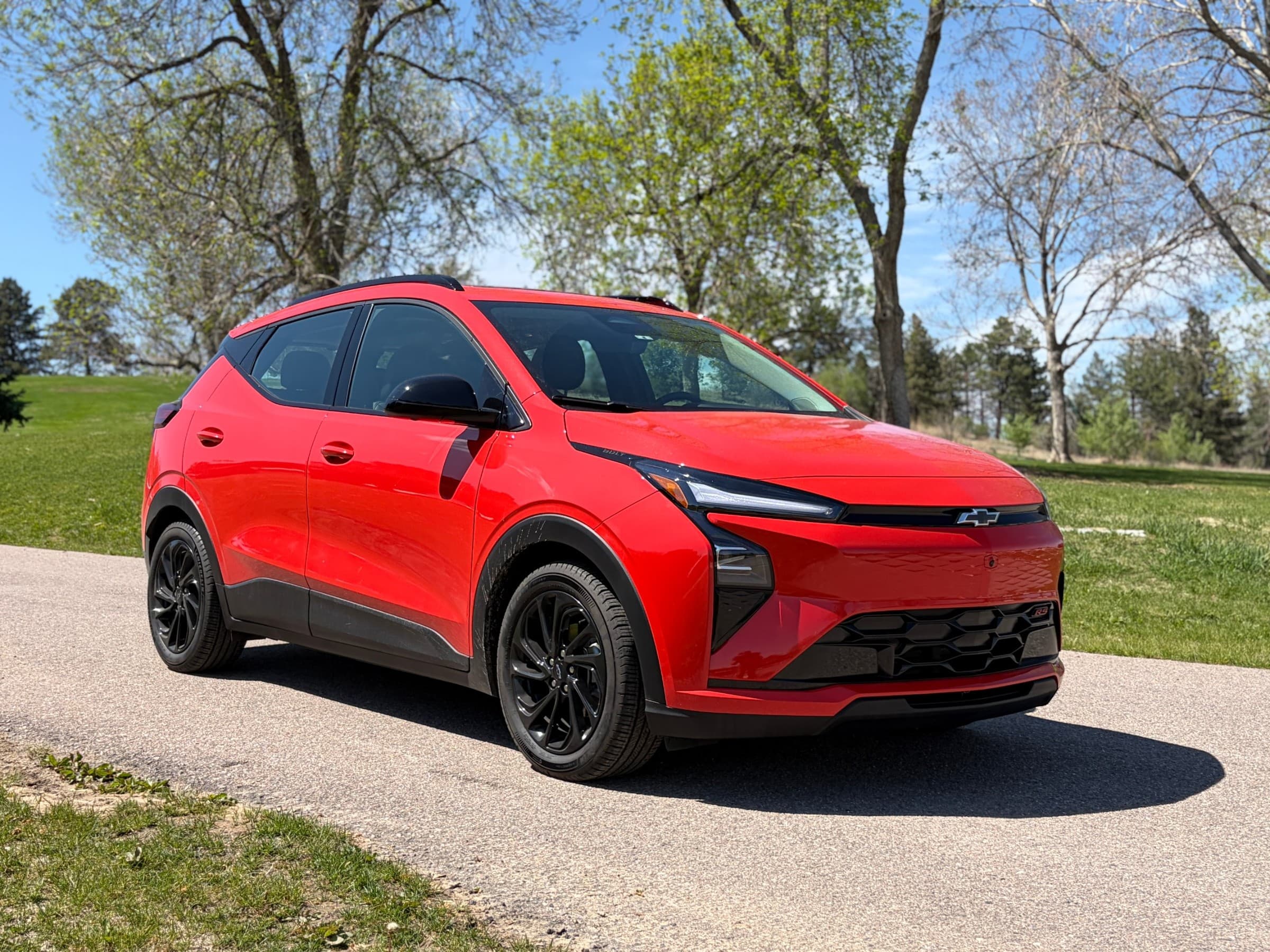 Rear three-quarter view of a red Chevrolet Bolt showing its black roof spoiler, slim taillights and Bolt badge on the liftgate.