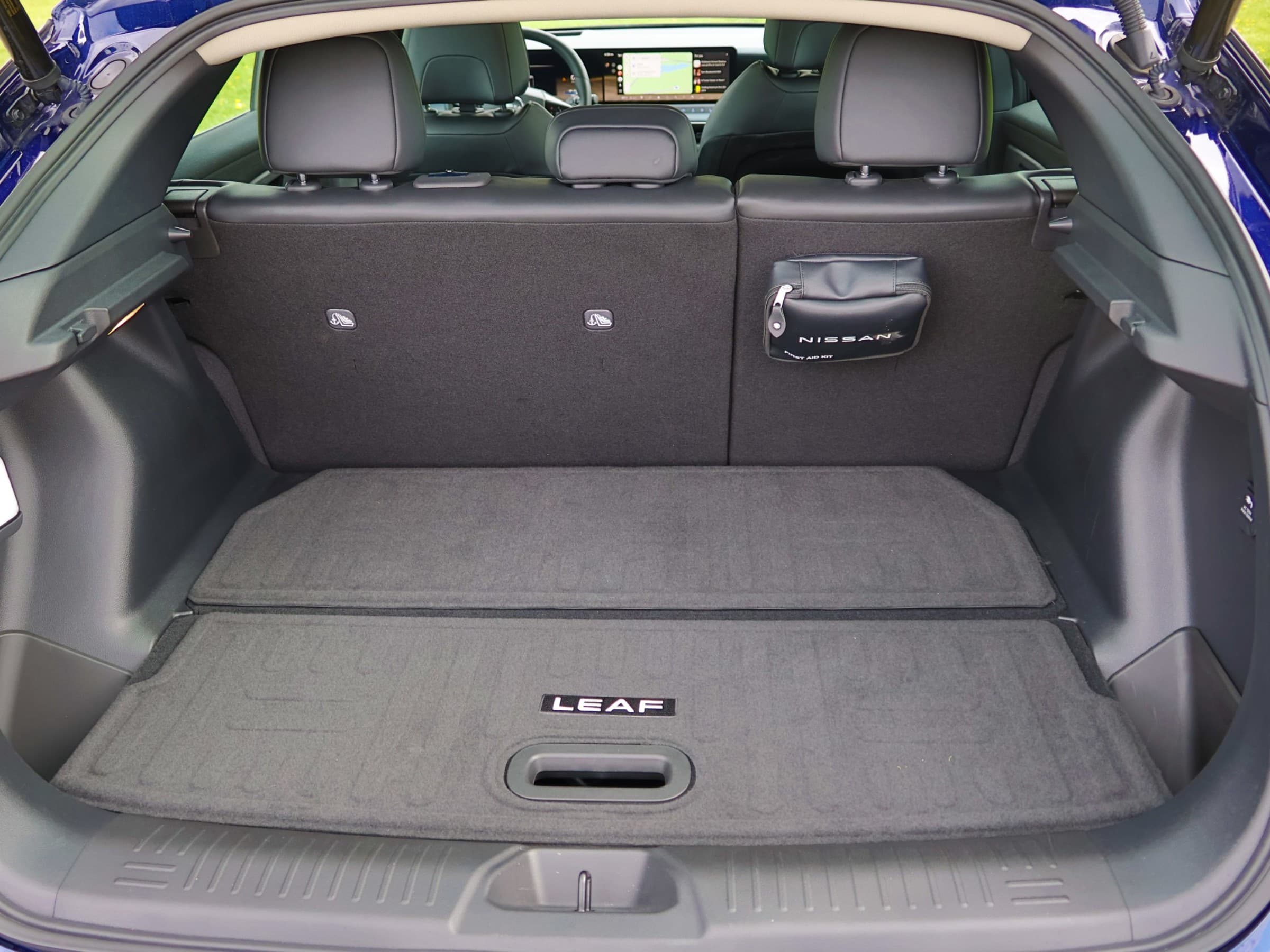 Cargo area of a Nissan Leaf with the hatch open, showing a carpeted load floor with a LEAF badge and the rear seatbacks upright.