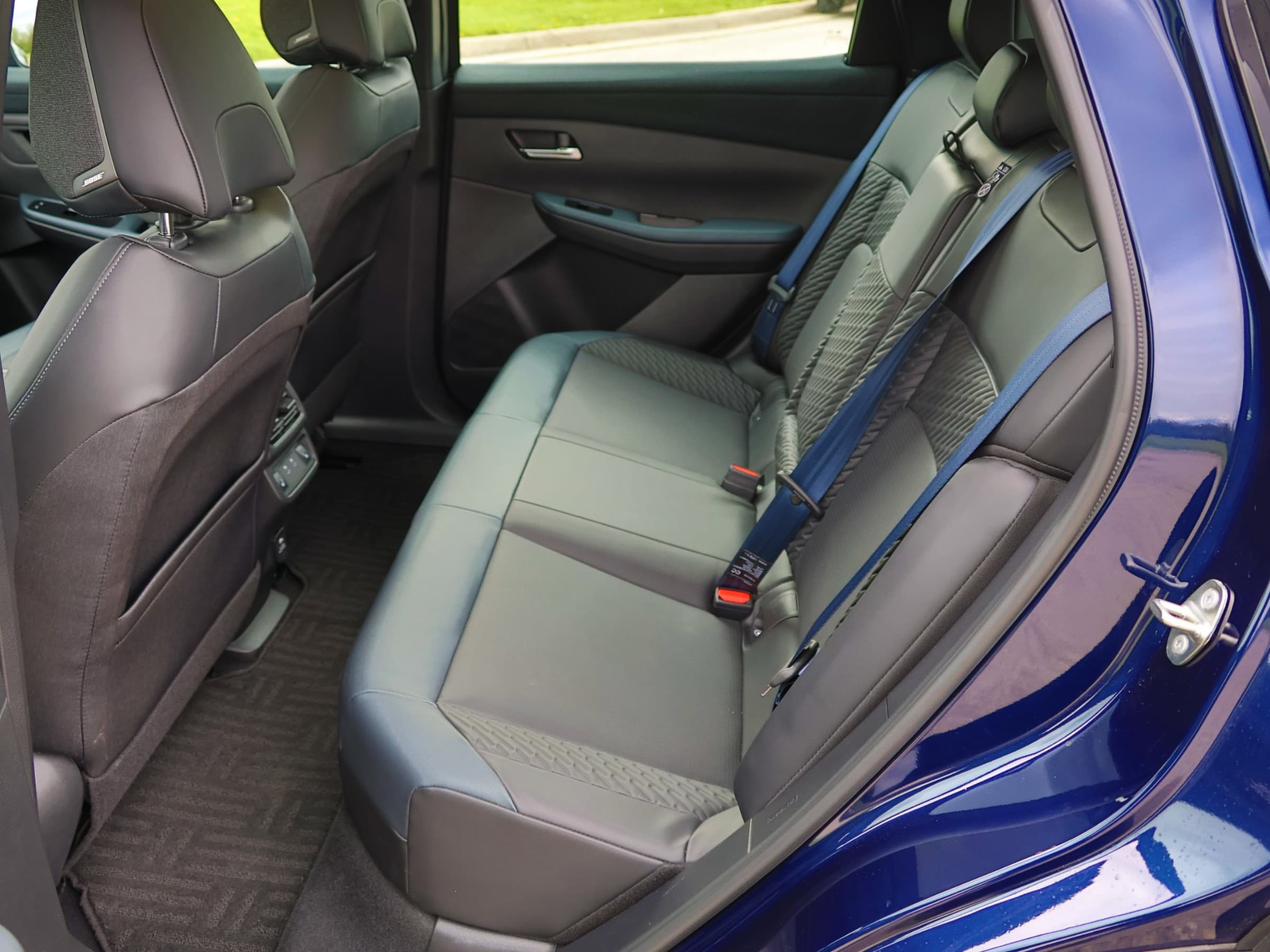 Rear seat of a Nissan Leaf viewed through the open back door, with gray textured upholstery and blue seatbelts.