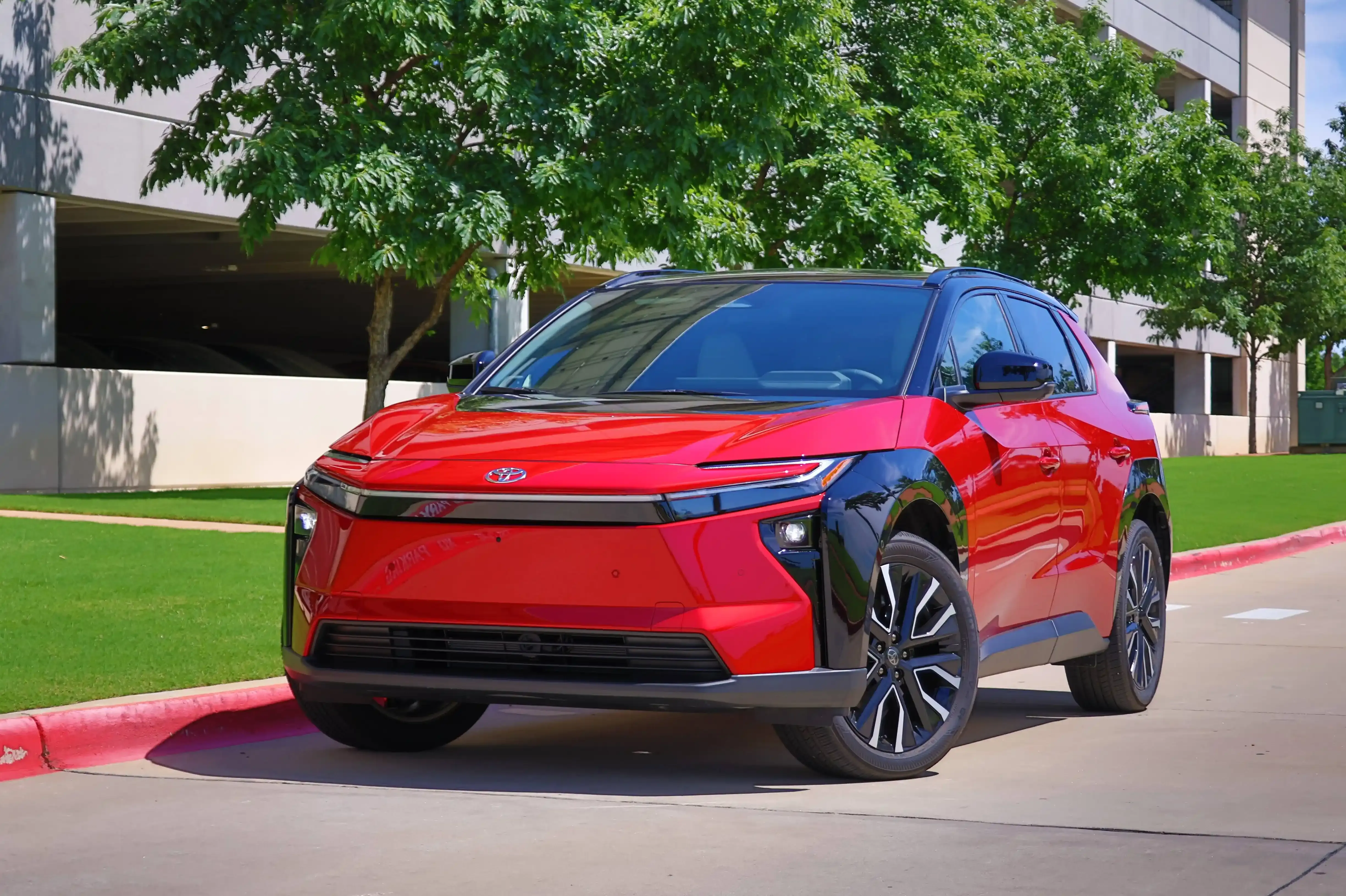 A red 2027 Toyota bZ electric SUV parked on a brick driveway with trees and a tan colored brick wall behind the vehicle