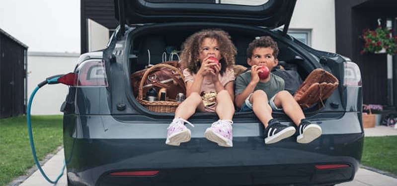 Children sitting in open trunk of car eating apples