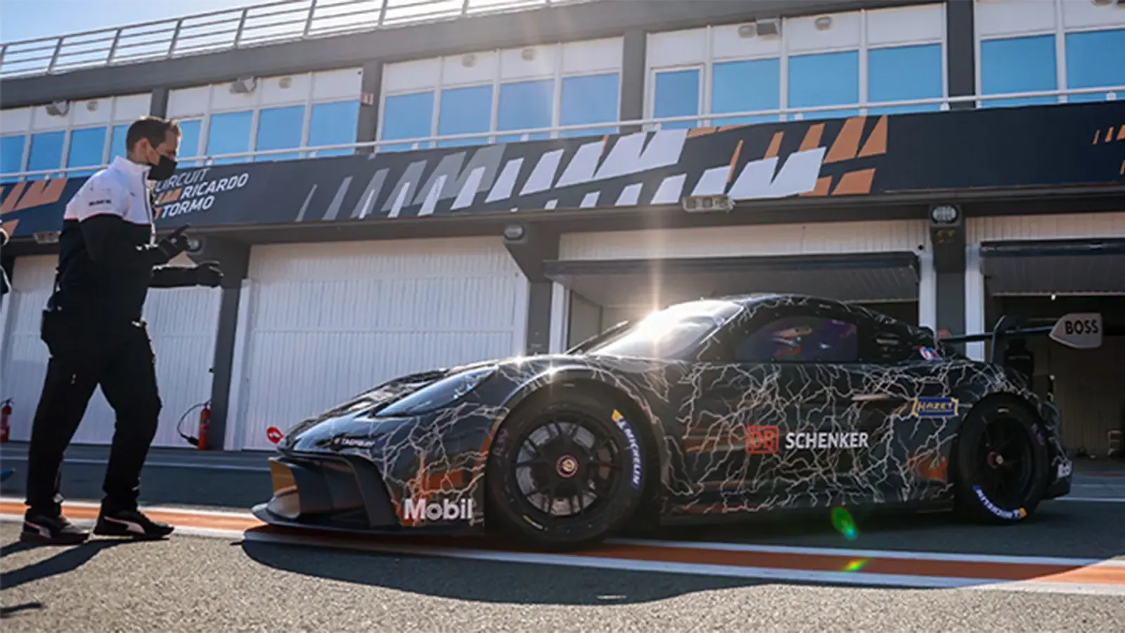 Porsche race car backing into garage with person directing