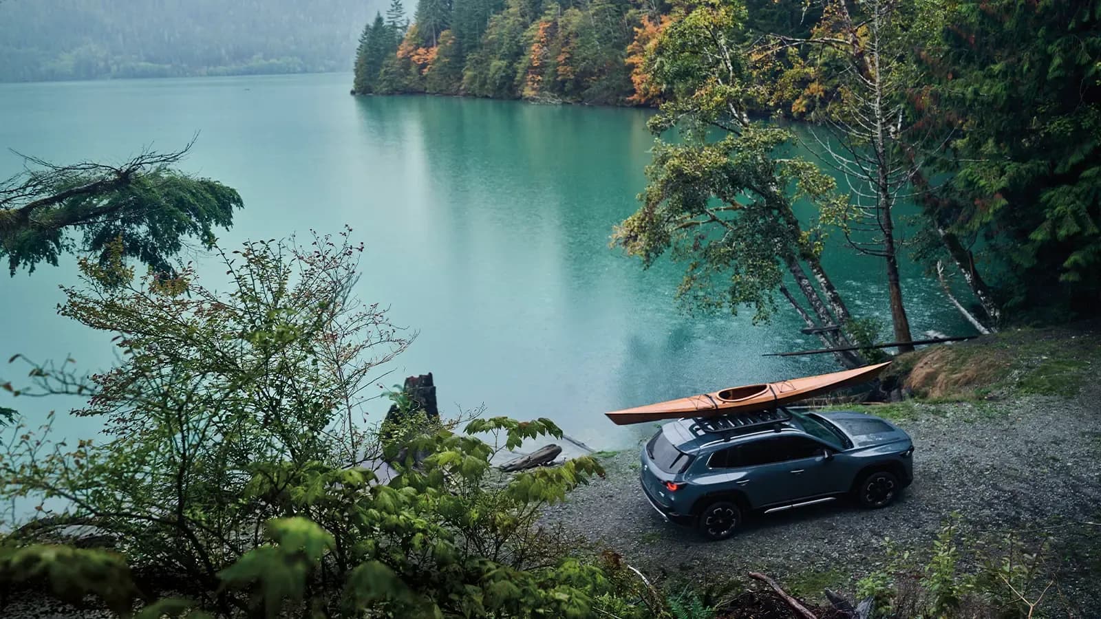 A Mazda SUV parked next to a lake surrounded by green forest