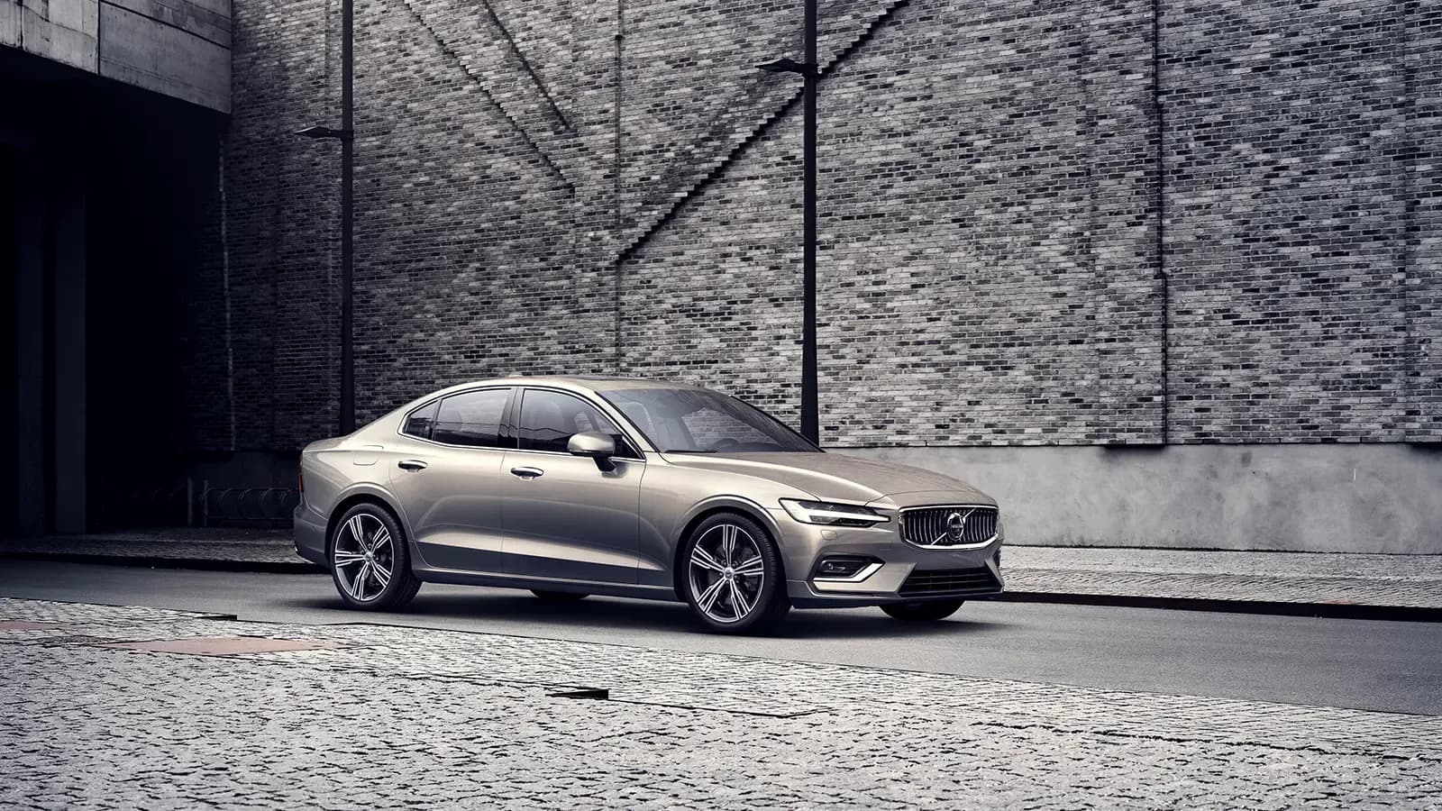 Volvo S60 Recharge driving in front of a brick wall