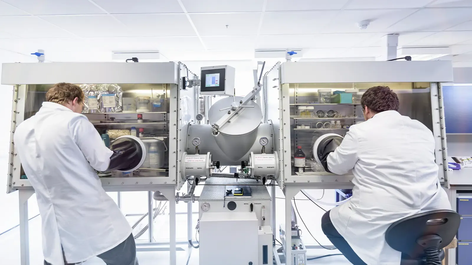 Scientists assembling batteries in glove chamber in battery research facility