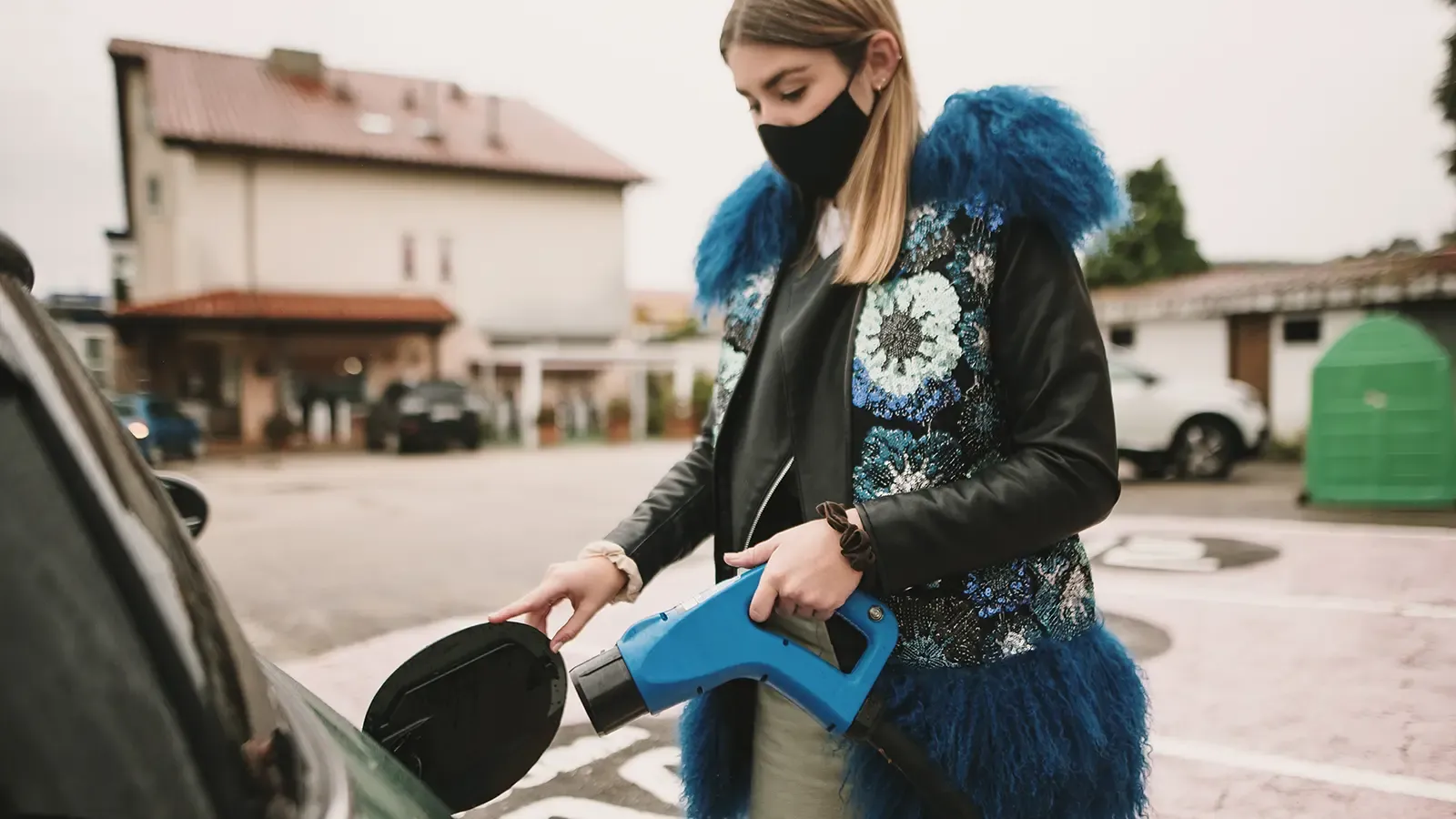 Masked woman charging her electric car