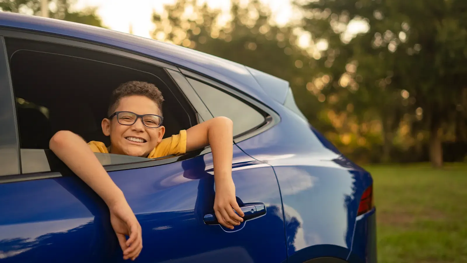 Kid hanging out the backseat window of a car, smiling