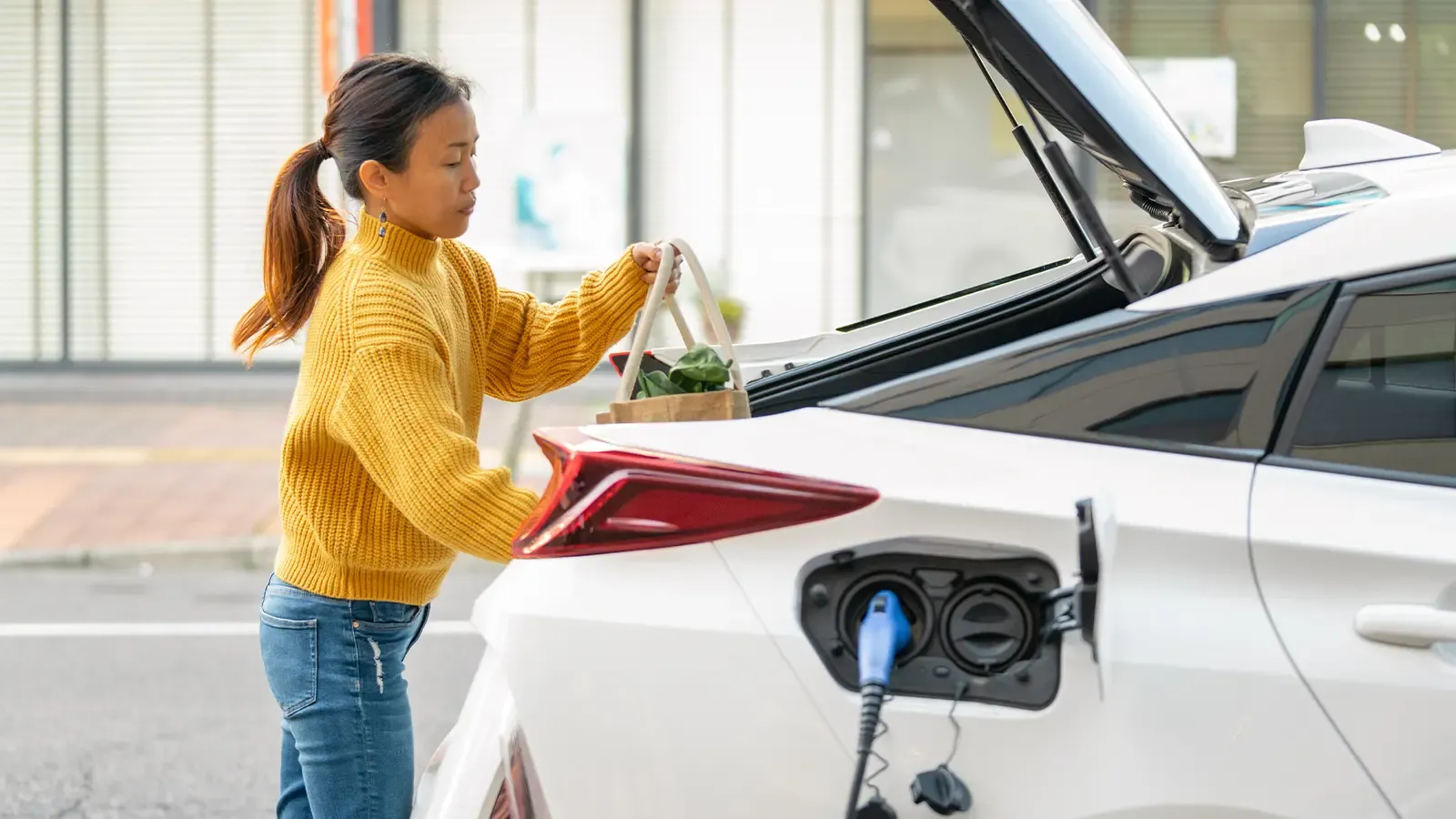 Woman putting groceries in trunk while car is charging
