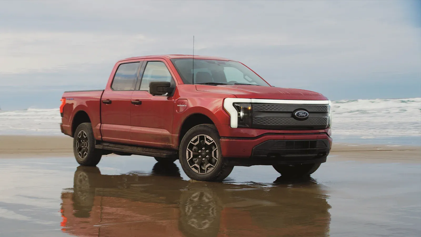 Red Ford F-150 Lightning parked along the beach in the sand with a hazy beach background