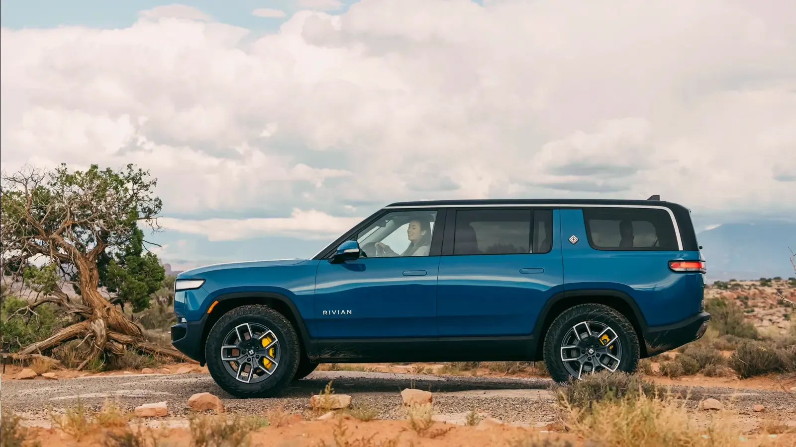 Rivian R1S SUV side profile in blue by a field