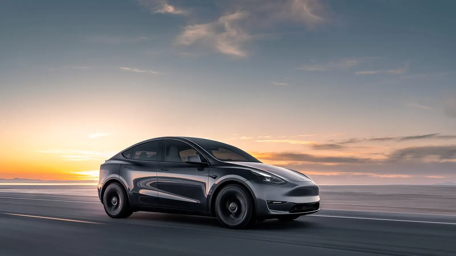 Black Tesla Model Y driving on a road by the sunset
