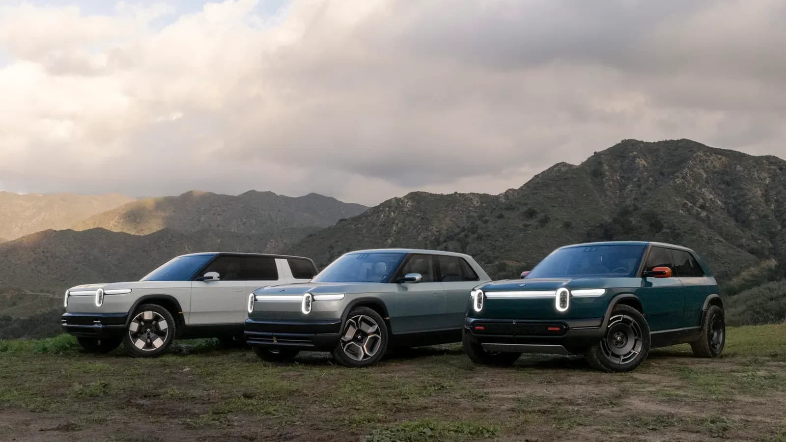 Rivian R2 and R3 parked side-by-side with cloudy skies and mountains in the background