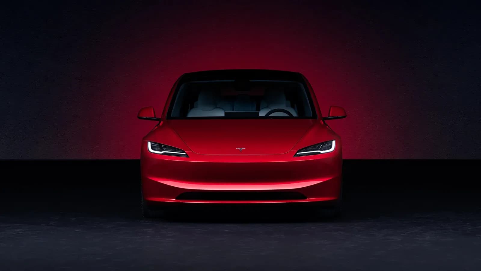 red Tesla EV parked in a dark room, with break lights glowing off the wall behind the vehicle