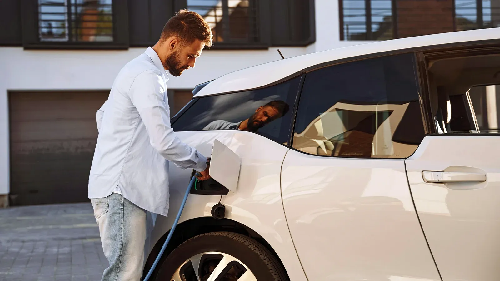 man plugging EV charger into white vehicle
