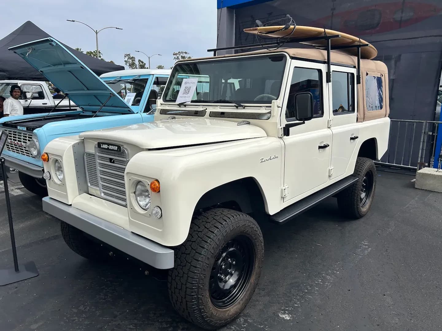Vista frontal en tres cuartos de una SUV todoterreno blanca con una tabla de surf en la parrilla del techo.