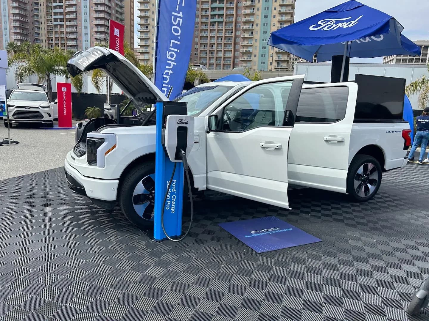 Vista frontal de tres cuartos de una camioneta eléctrica blanca cargando con el frunk y las puertas abiertas.