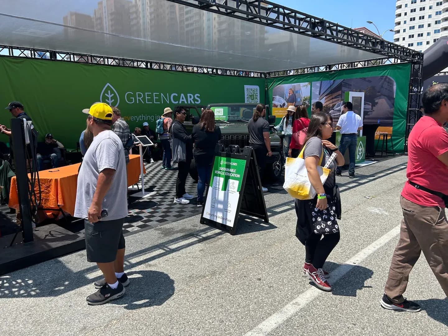Varias personas se reúnen alrededor de un stand de GreenCars con un SUV tipo Jeep bajo una carpa.