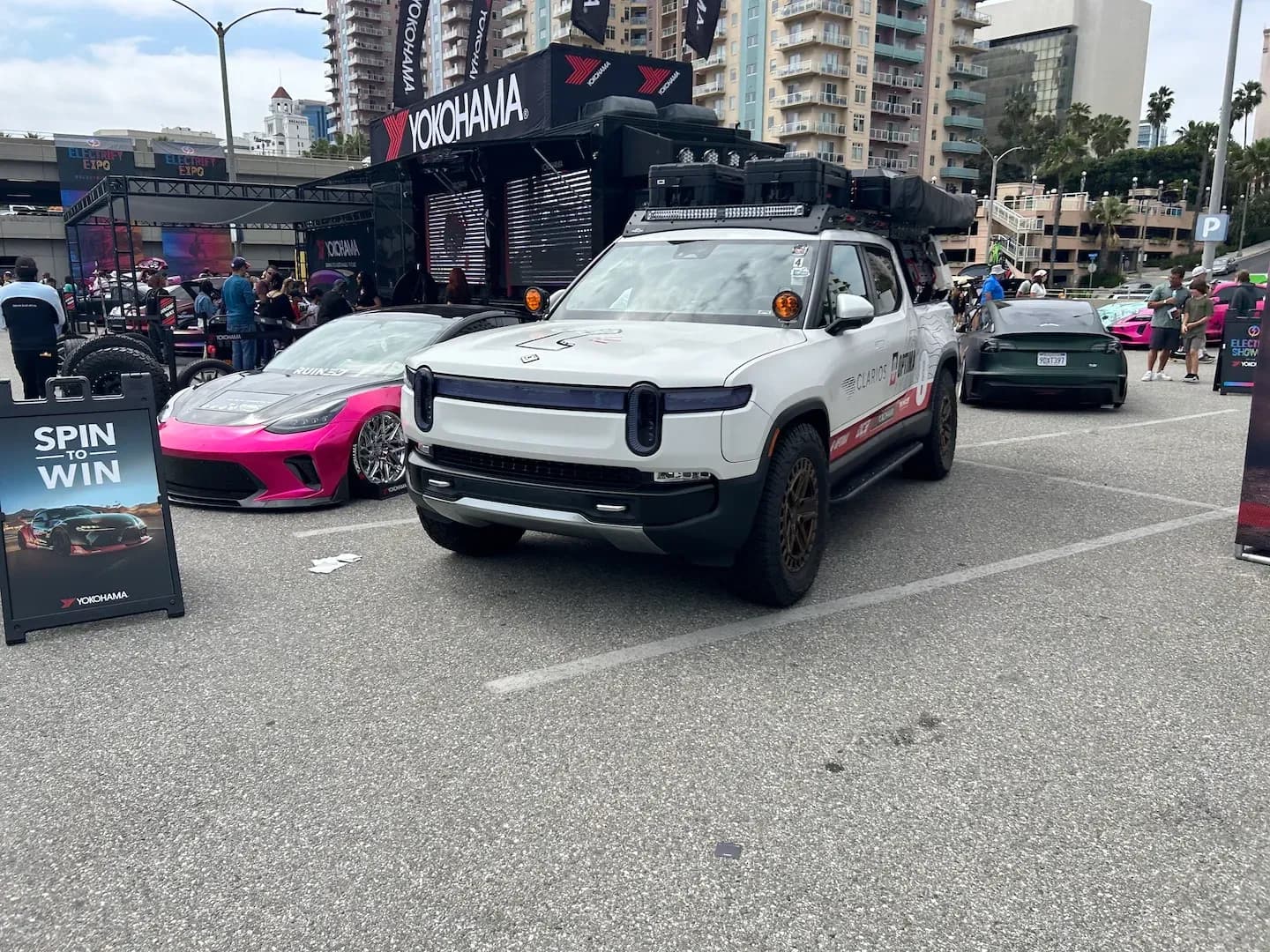 Vista frontal de tres cuartos de una camioneta eléctrica blanca con equipo en el techo en una exhibición de Electrify Expo.