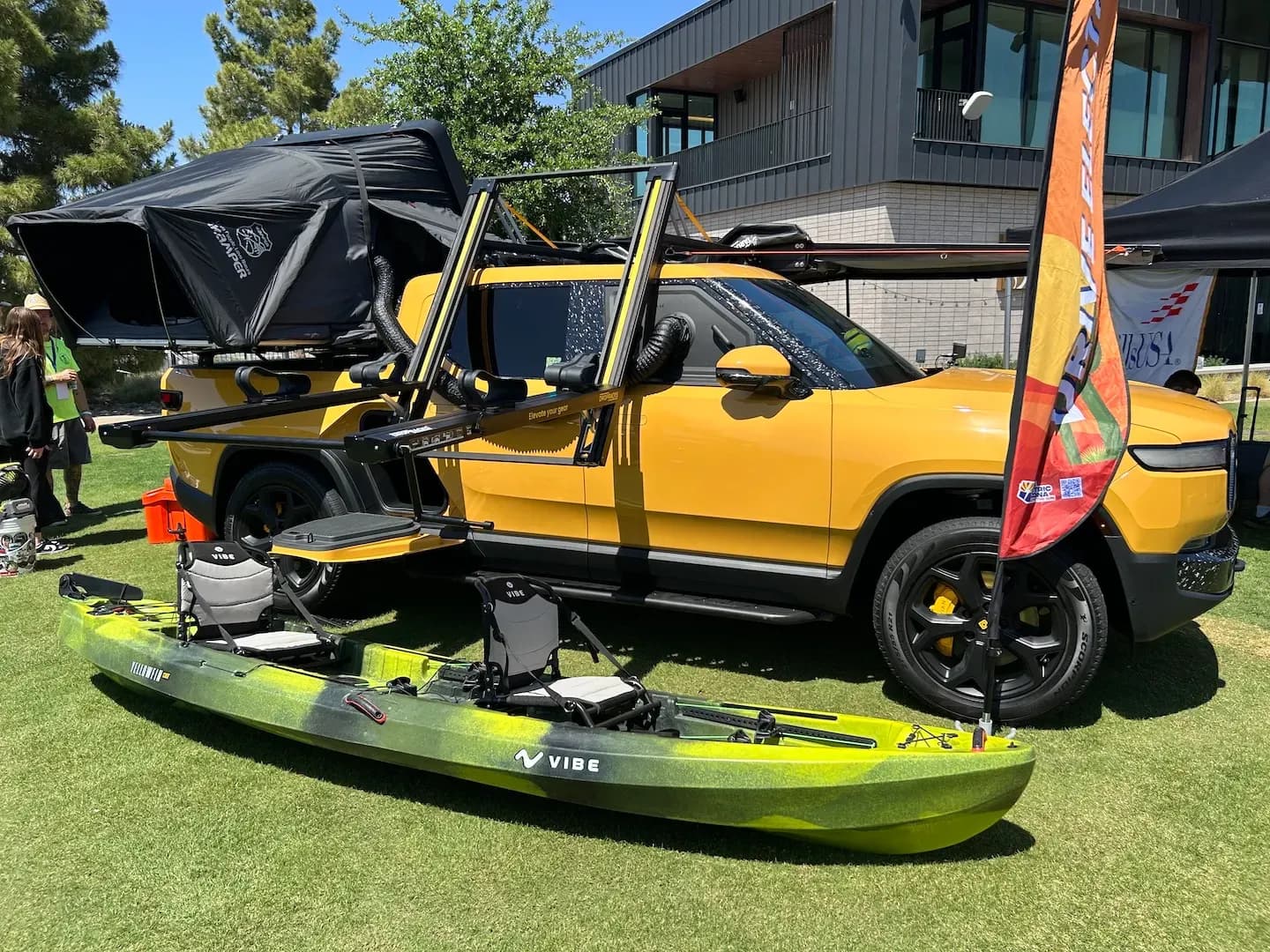 Pickup eléctrica amarilla con una tienda de techo, un kayak y equipo de campamento en exhibición.