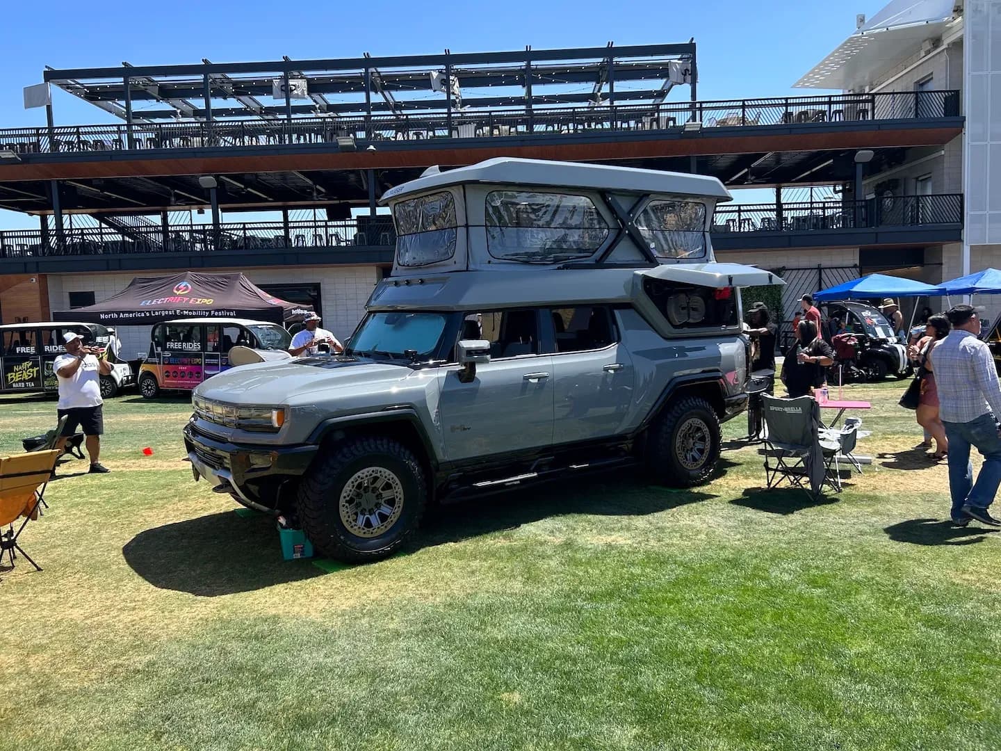 Vista delantera en tres cuartos de una pickup eléctrica gris con una tienda de techo desplegable en una expo.