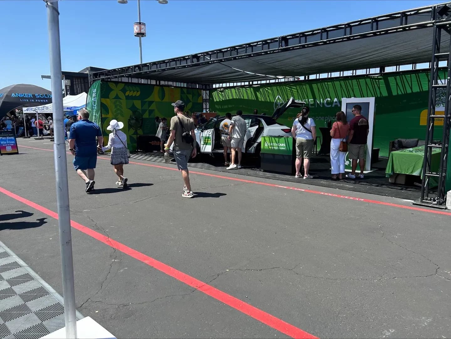 Vista amplia del stand de GreenCars en la expo, con personas reunidas alrededor de una SUV blanca en exhibición.