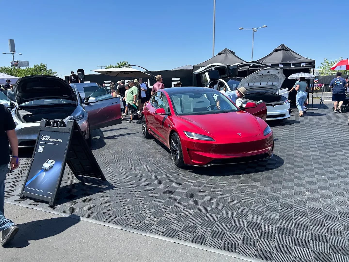 Vista frontal de una berlina eléctrica roja en una expo de vehículos eléctricos al aire libre, con las puertas abiertas.