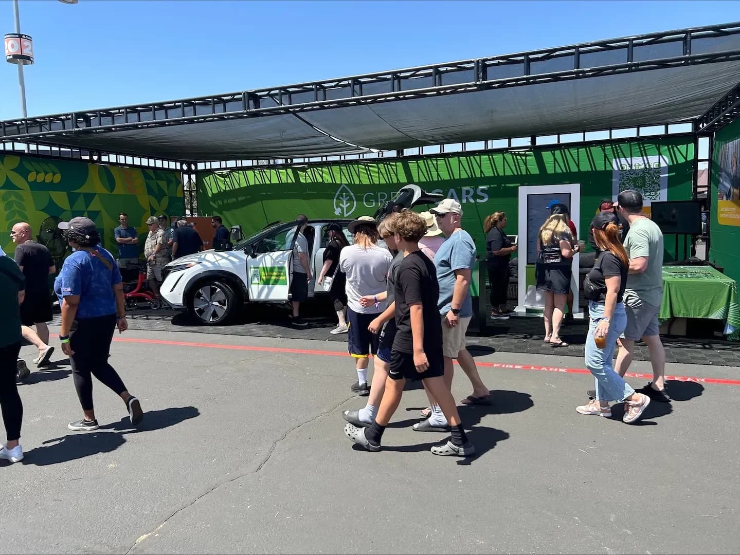 Personas pasan junto a un stand de GreenCars con un SUV eléctrico blanco en exhibición.