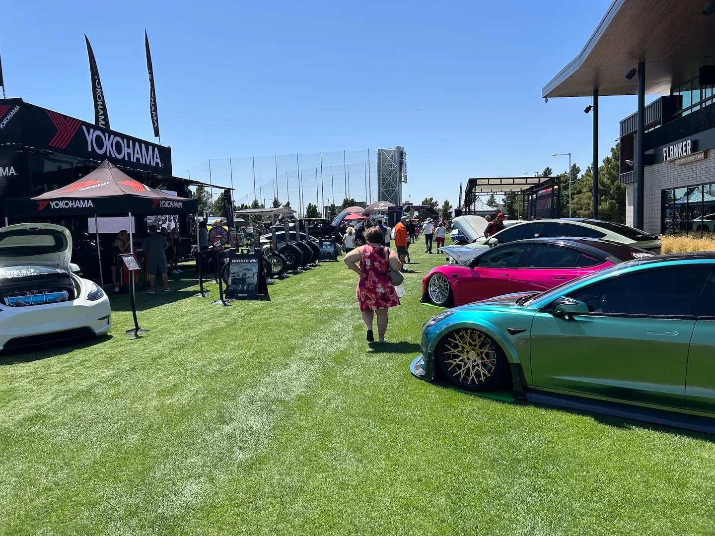 Amplia exhibición al aire libre con autos eléctricos personalizados, carpas y una persona caminando sobre el césped.