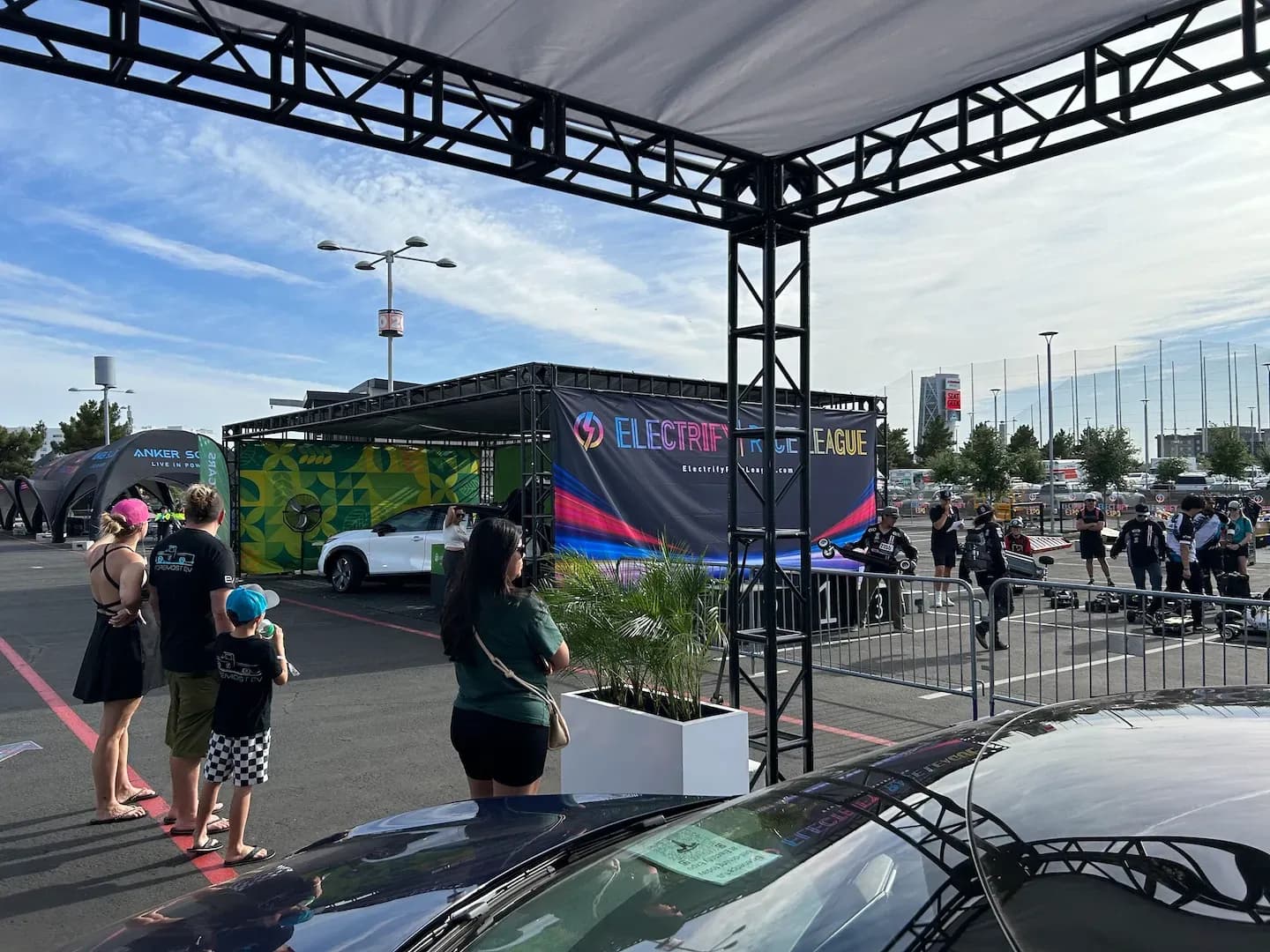 Varias personas observan un área de carrera junto a un display de Electrify Expo League y una SUV eléctrica blanca.