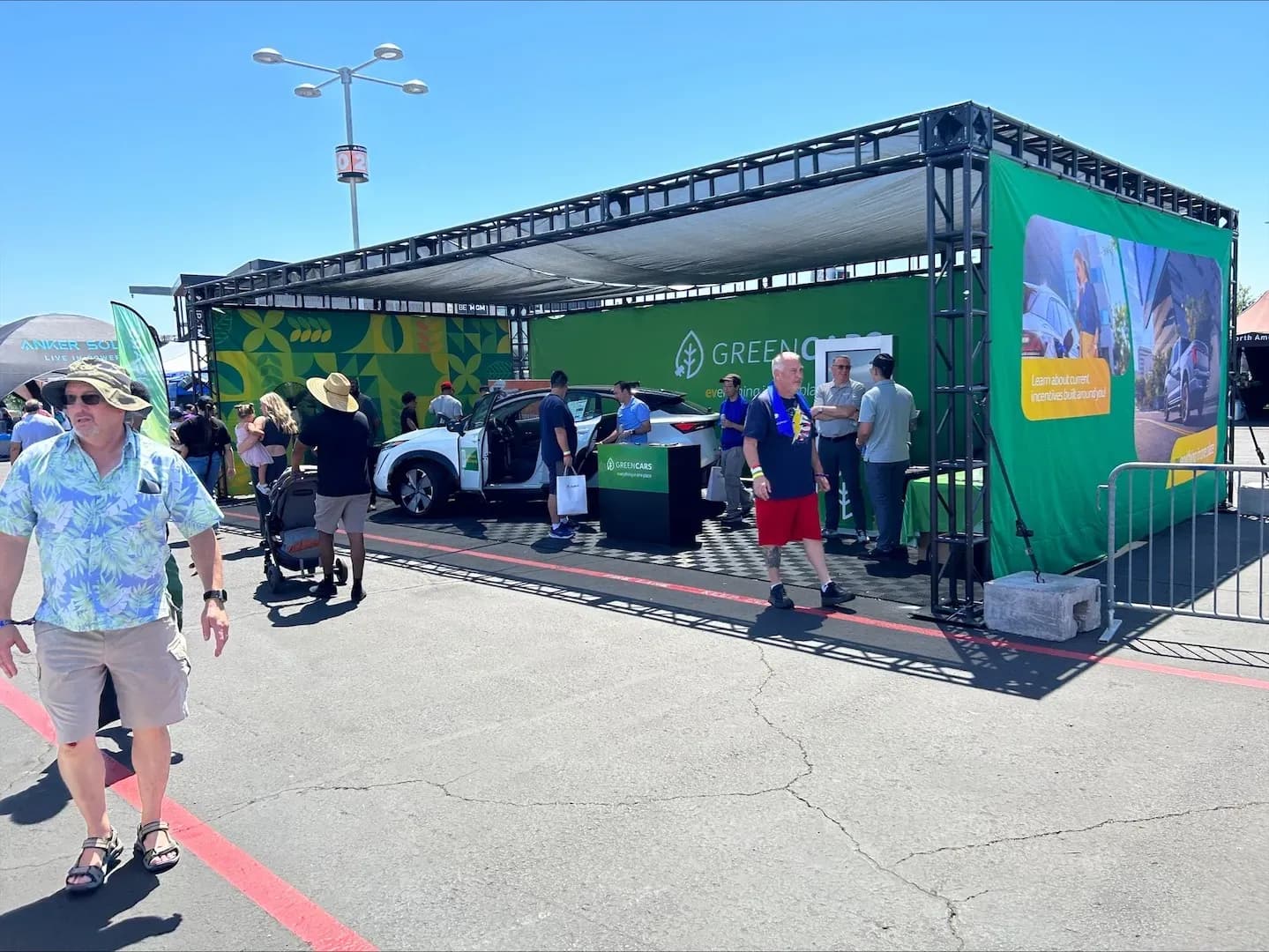 Varias personas se reúnen alrededor de un SUV eléctrico blanco en el stand de GreenCars.
