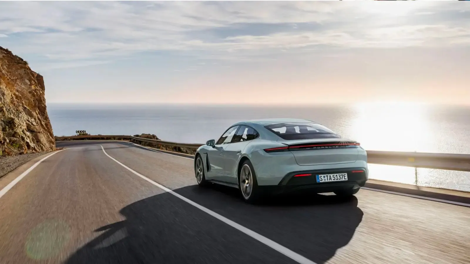 Porsche Taycan exterior back view driving on a road by the sea