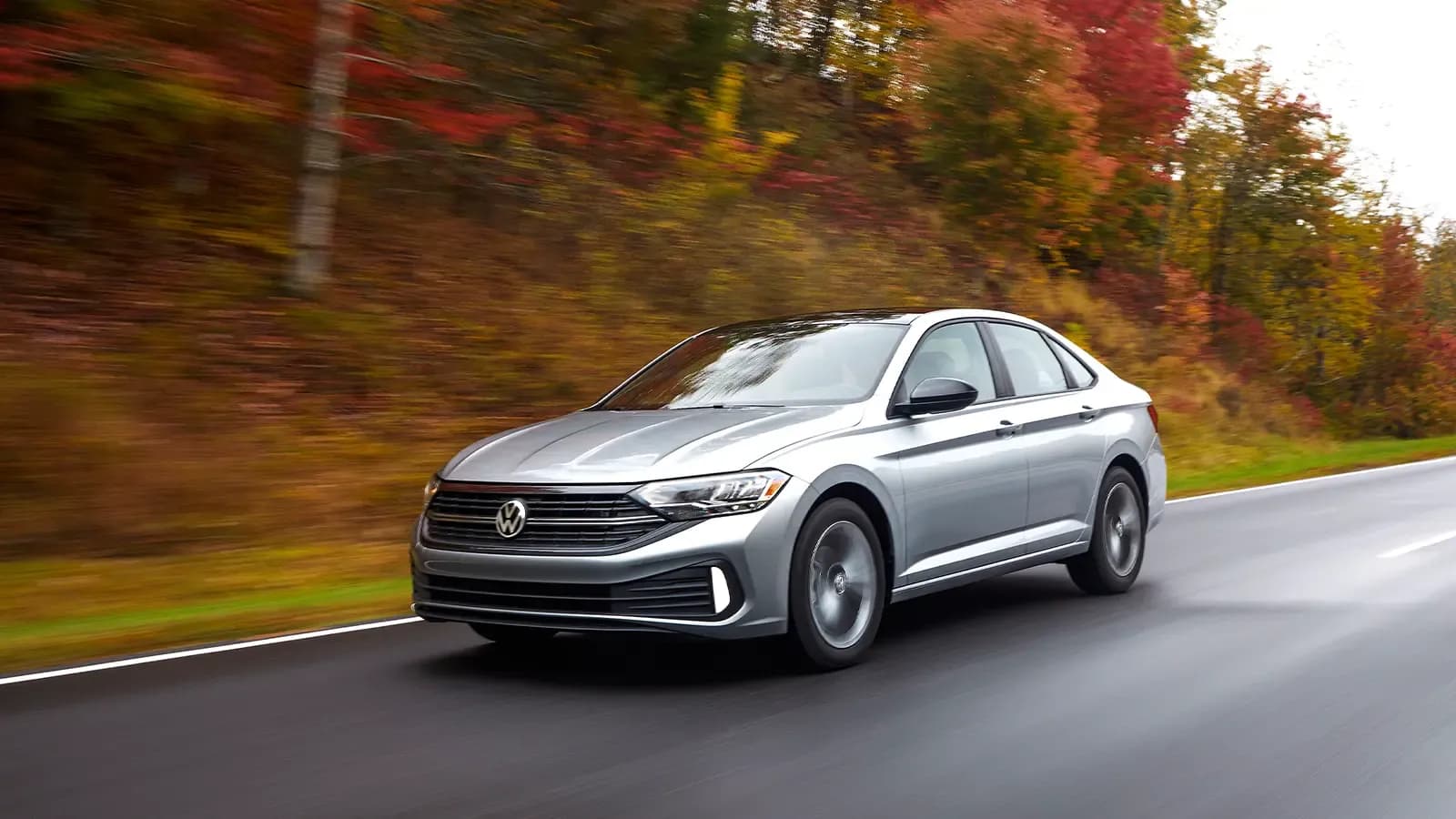 Volkswagen Jetta driving with fall trees