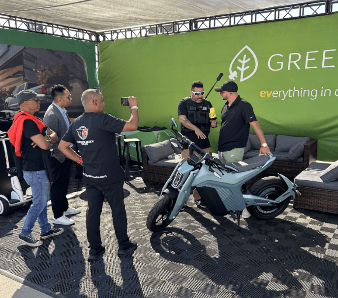 Varias personas se reúnen alrededor de un scooter eléctrico azul claro en el stand de GreenCars.