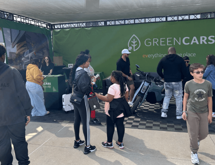 Varias personas se reúnen alrededor de una motocicleta en un stand de GreenCars en Electrify Expo.