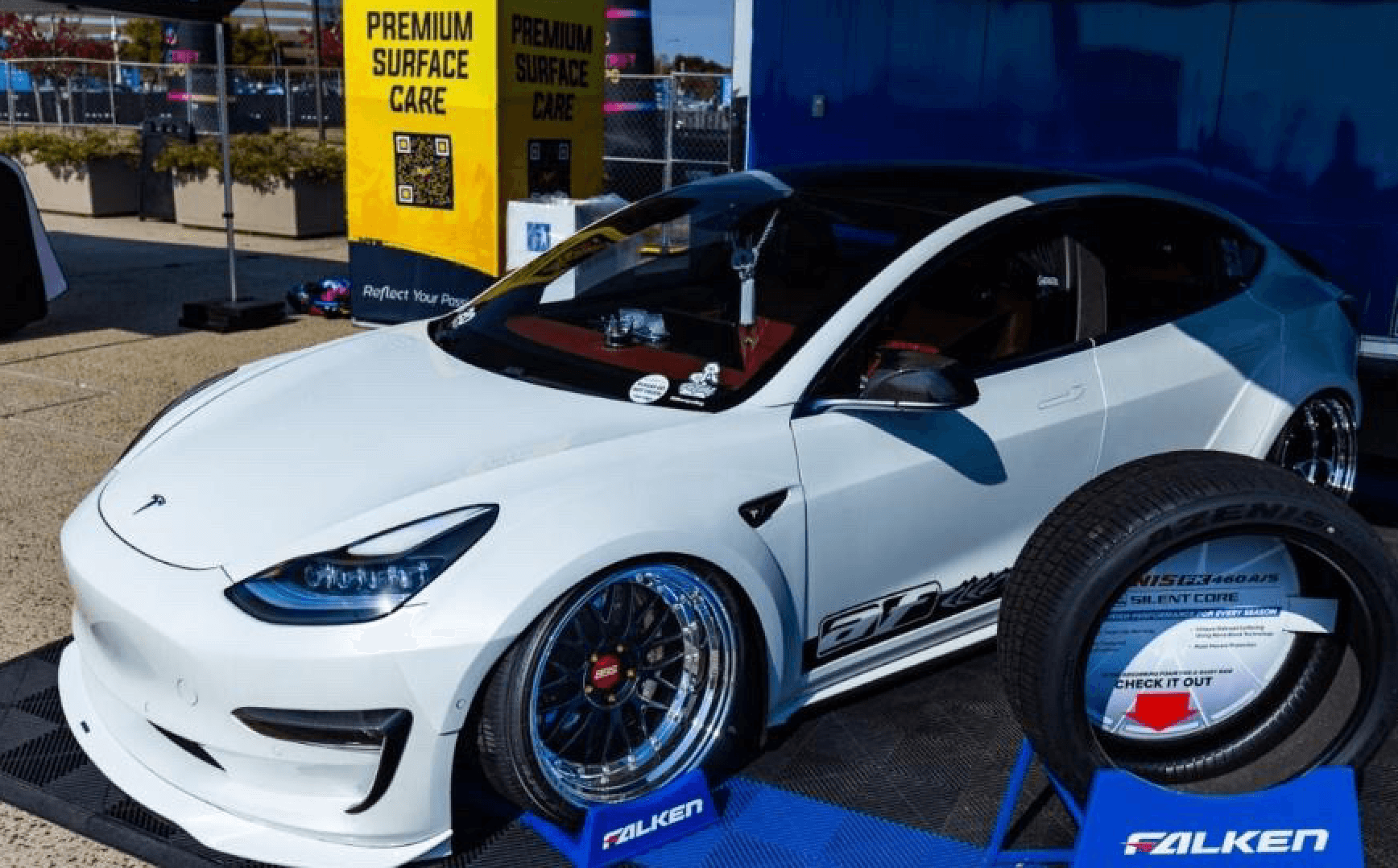 Sedán eléctrico blanco en exhibición con rines grandes de posventa y postura baja.