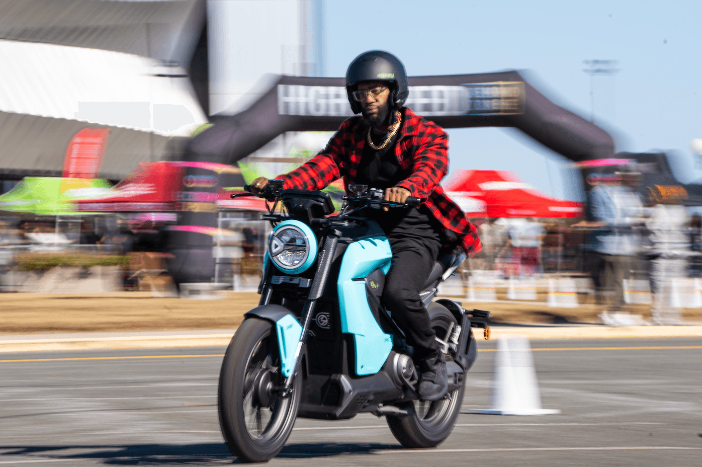 Una persona maneja una motocicleta eléctrica azul claro en un evento al aire libre.
