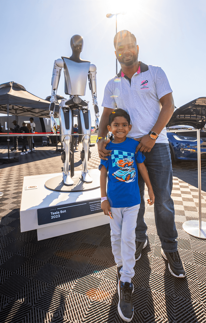 Un hombre y un niño posan frente a una exhibición de un robot humanoide en una expo al aire libre.