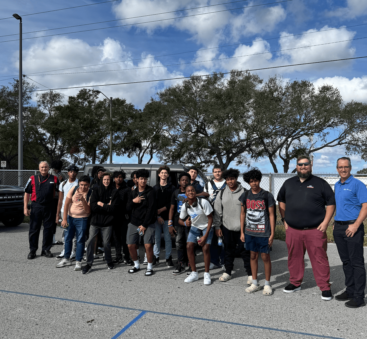 Group of students and adults standing outdoors beside a parked SUV and truck.