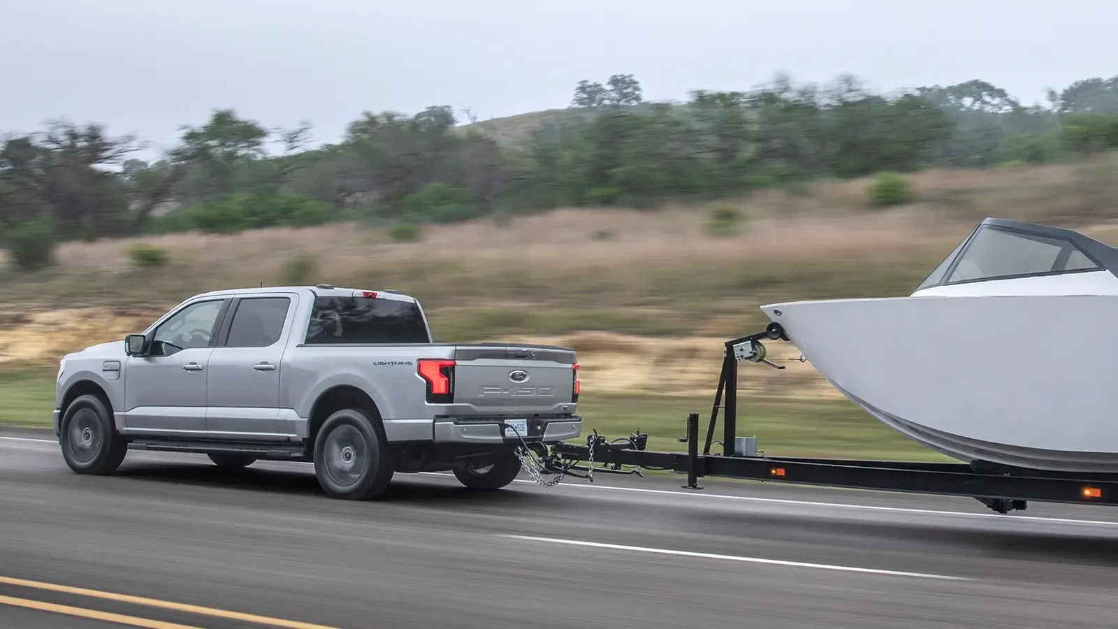 Silver ford f-150 towing a boat through forest