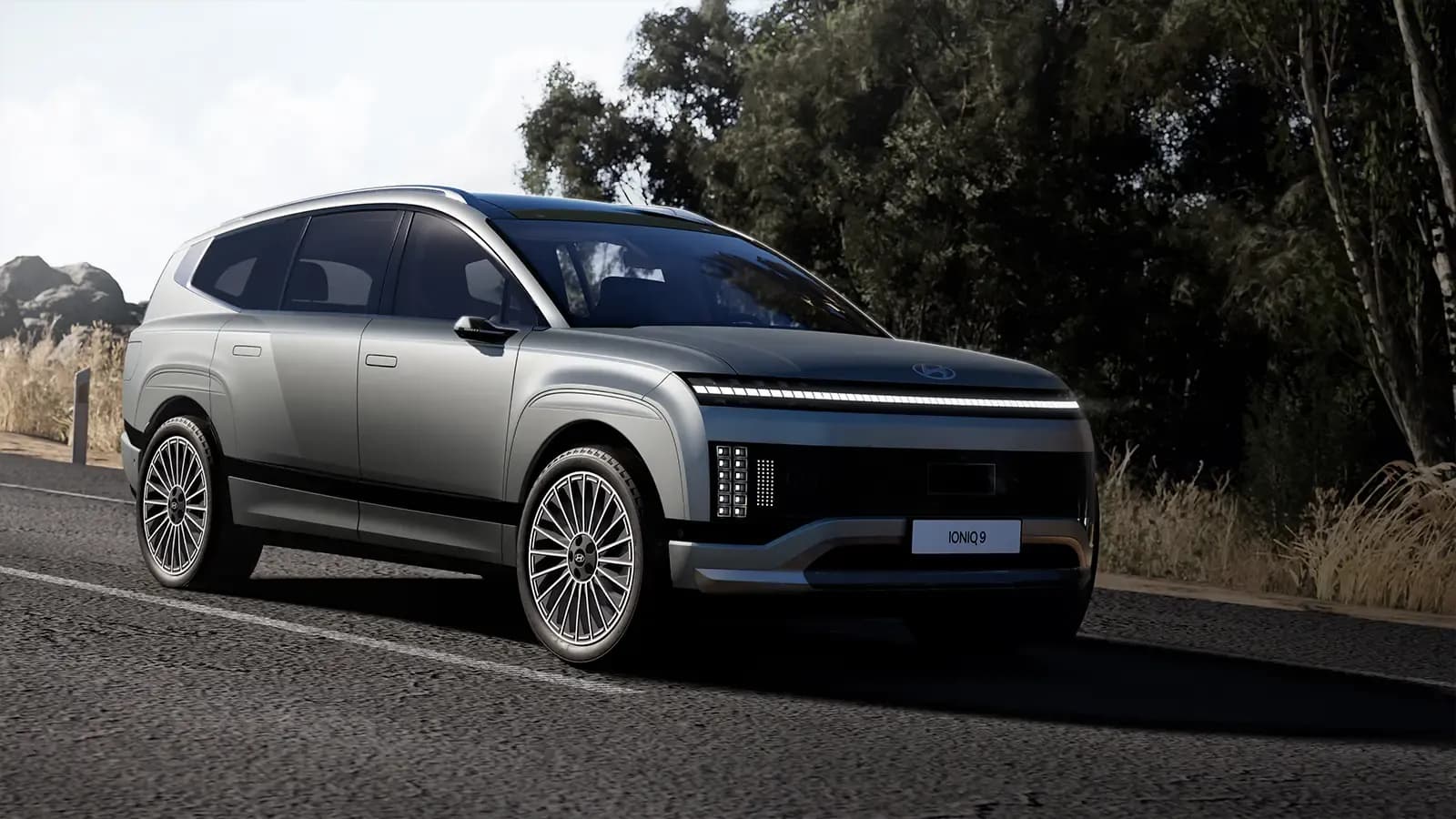 Vista frontal de tres cuartos de un SUV Hyundai Ioniq 9 plateado circulando por una carretera.