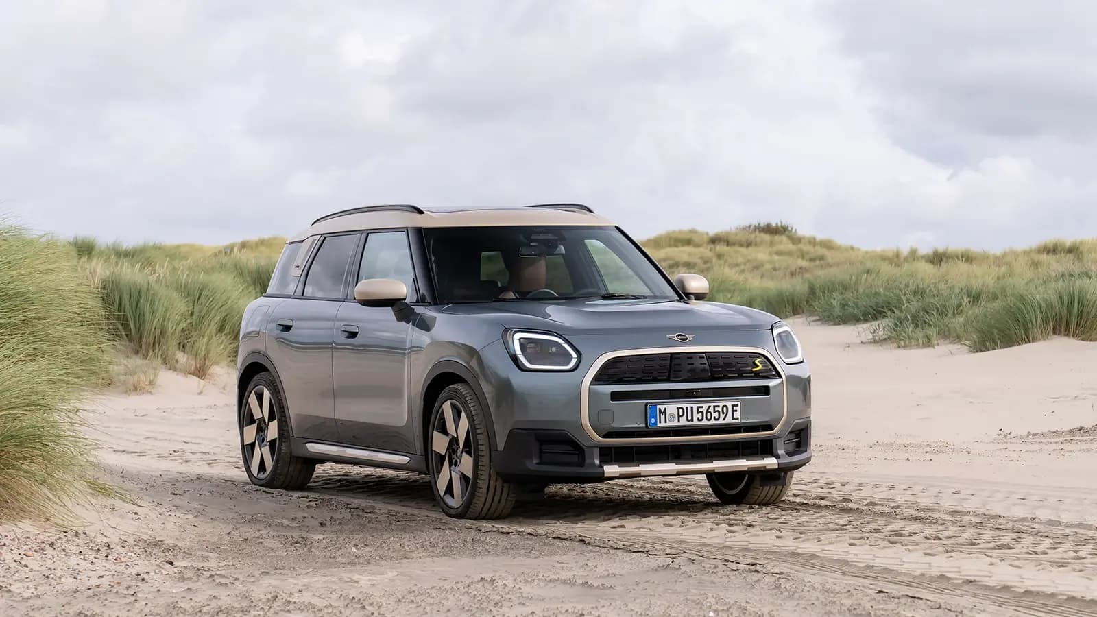 Vista frontal de tres cuartos de un Mini Countryman SE gris sobre dunas de arena.