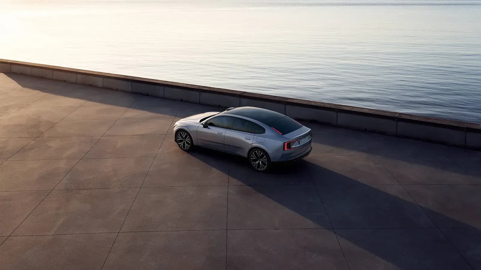 Silver Volvo ES90 parked near calm waters