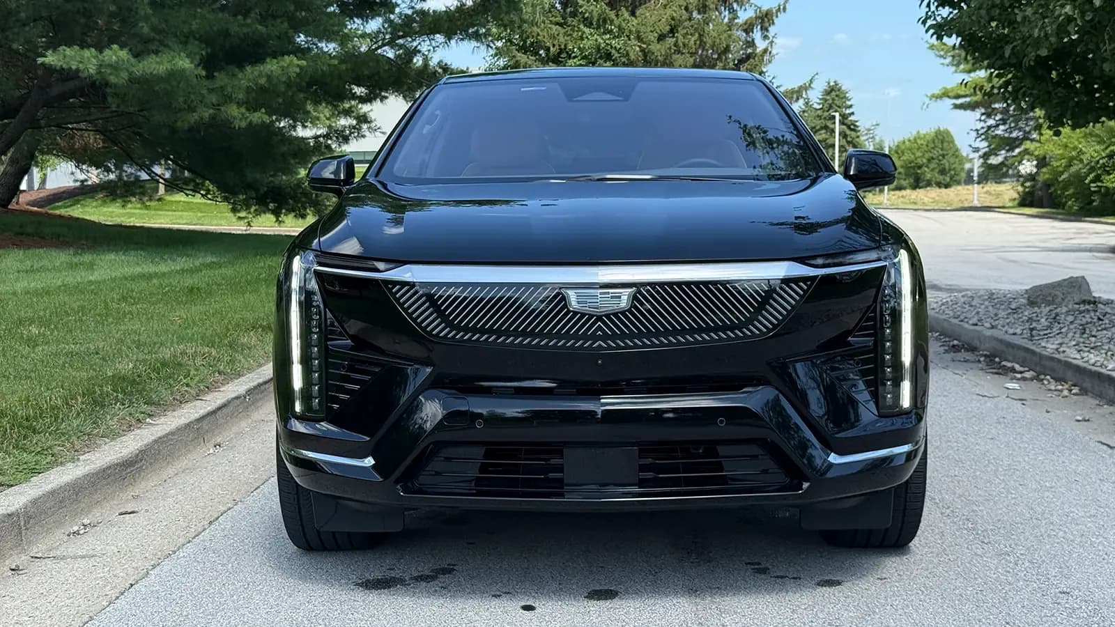 Front view of a black Cadillac Optiq with vertical LED headlights parked on a road.