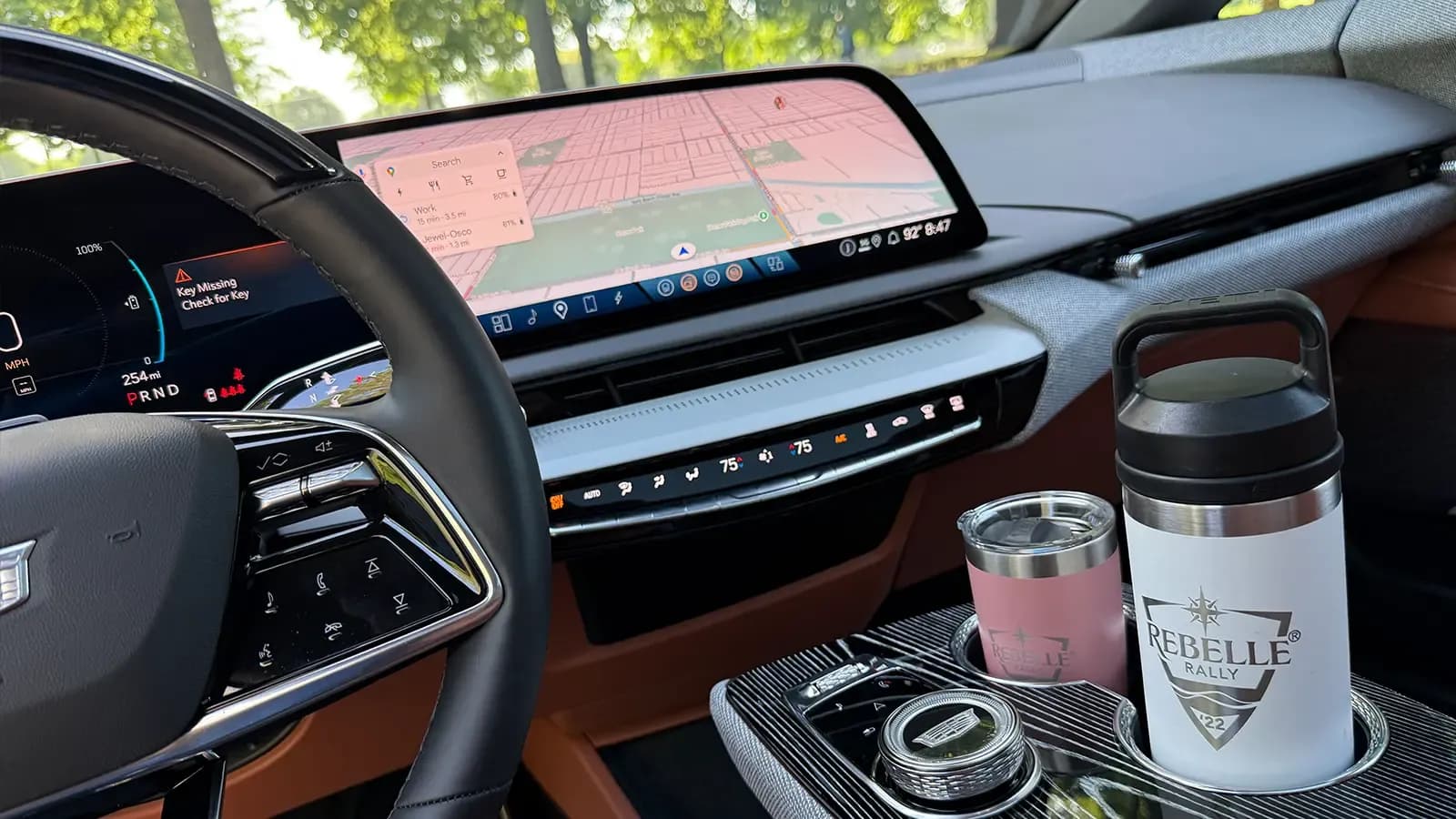 Cadillac Optiq interior with digital gauges, navigation screen, and two drink tumblers in the center console.