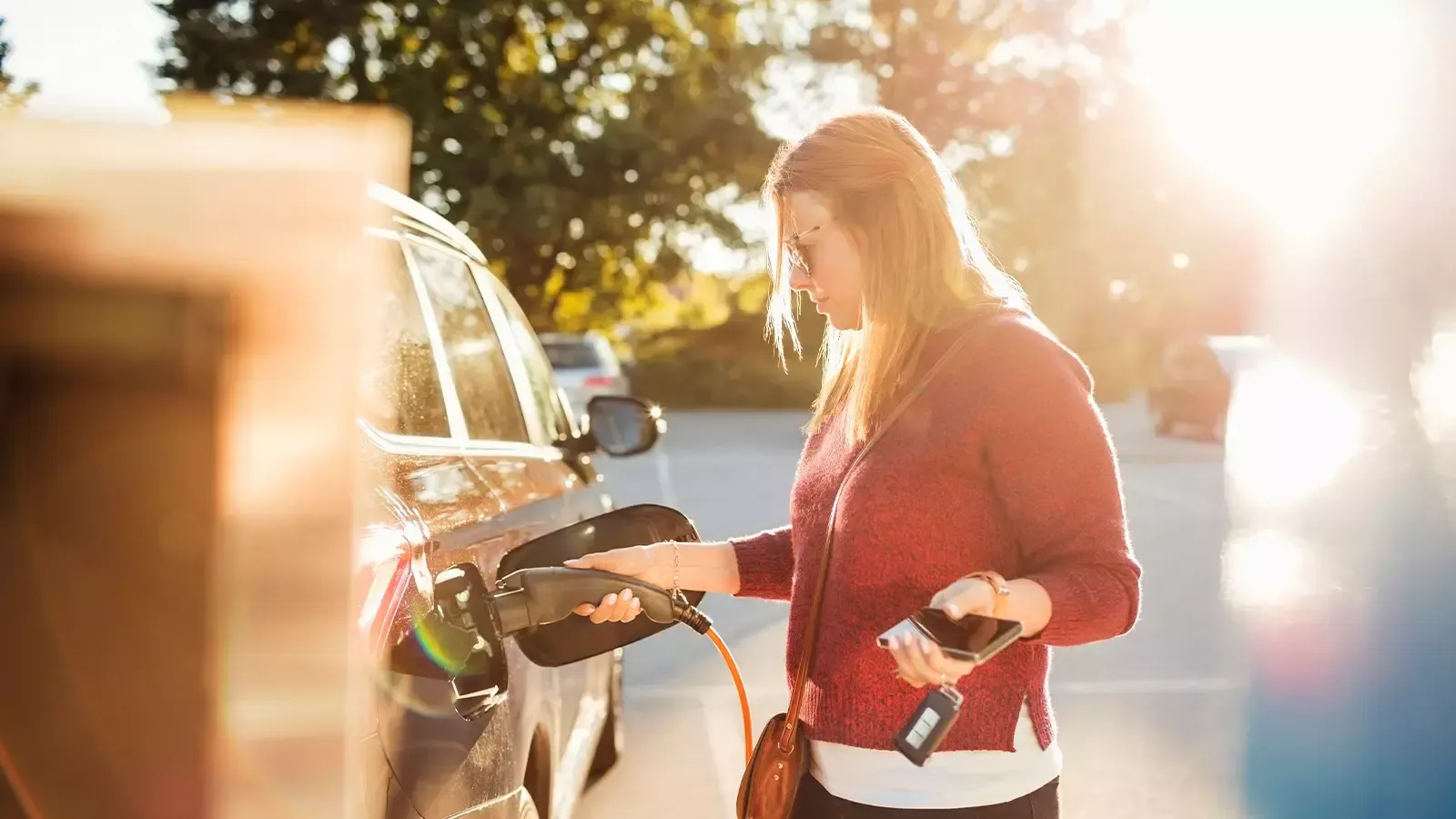 Woman charging an EV car in bright afternoon sunlight